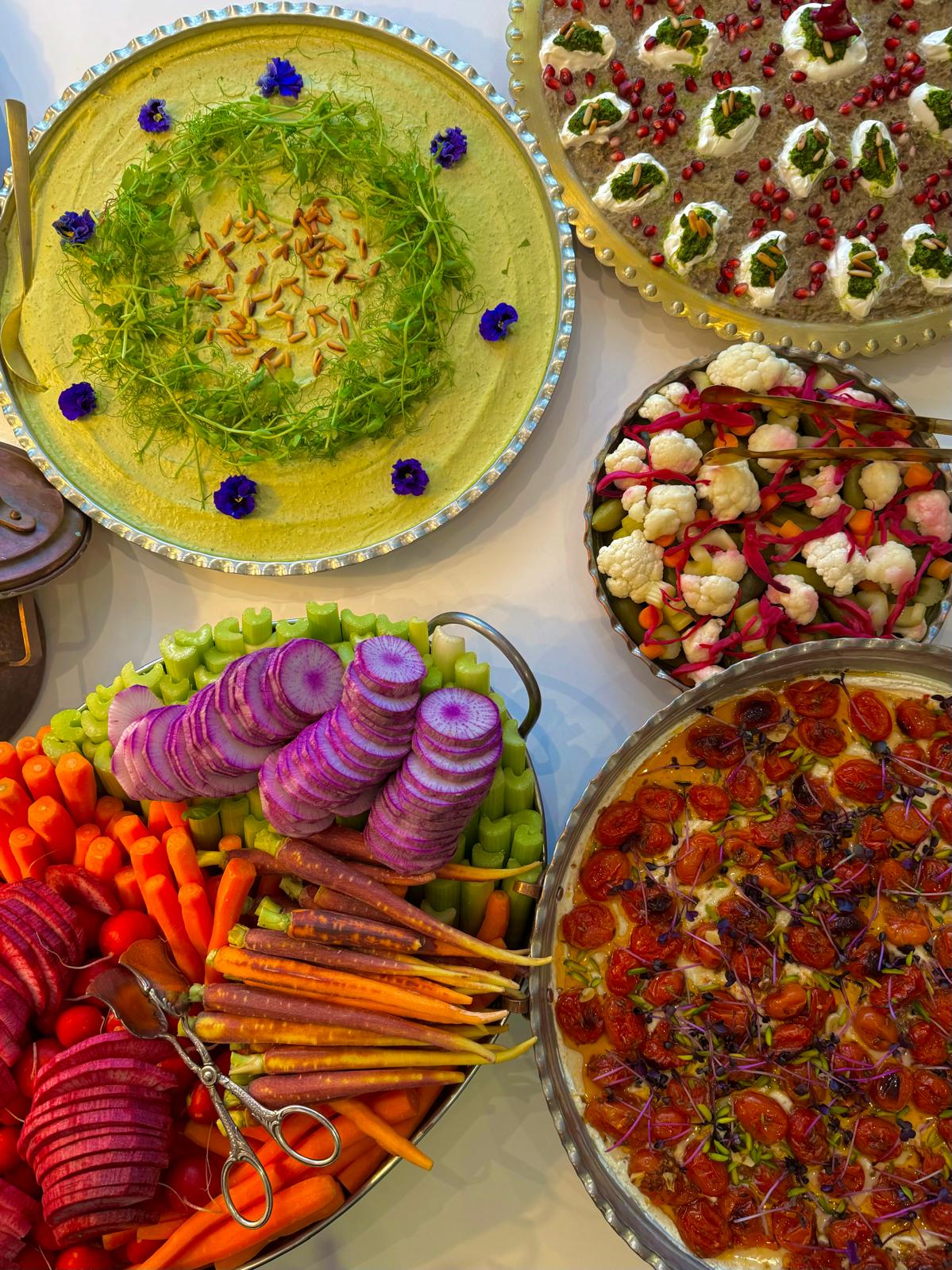 Various oriental appetizers on round plates, including hummus with pine nuts and flowers, roasted vegetables, pickled vegetables, yogurt dip with pomegranate and colorful carrots and radishes