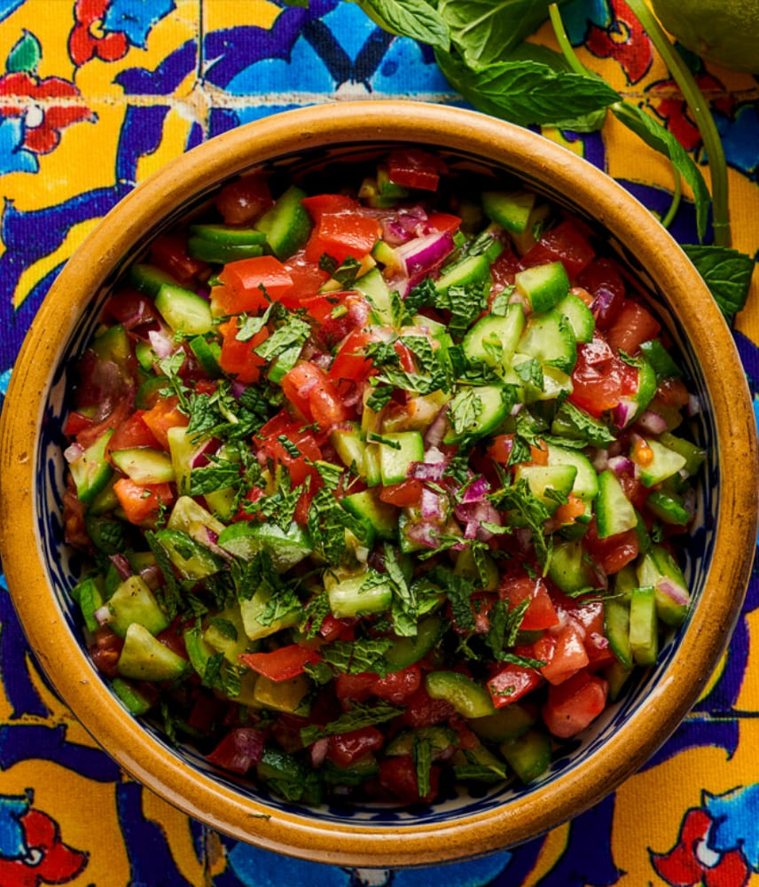 Colorful bowl with freshly prepared Persian Shirazi salad made of tomatoes, cucumbers, red onions, and chopped herbs on an oriental patterned cloth.